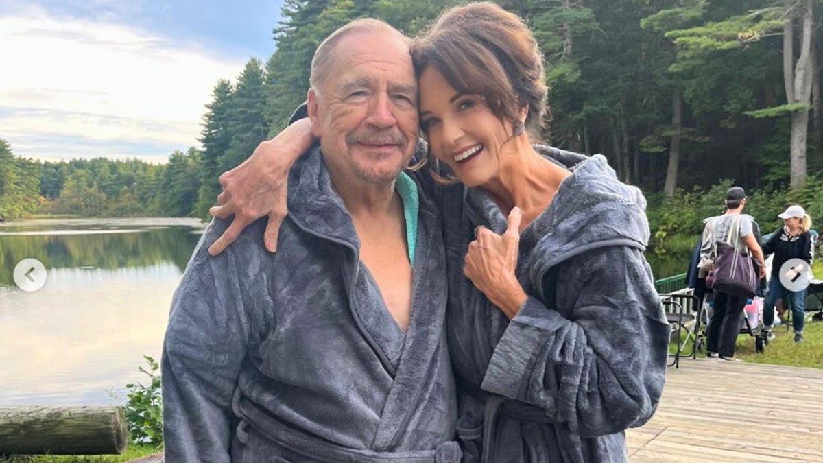 Lynda Carter posing in a gray robe with her co-star on set of