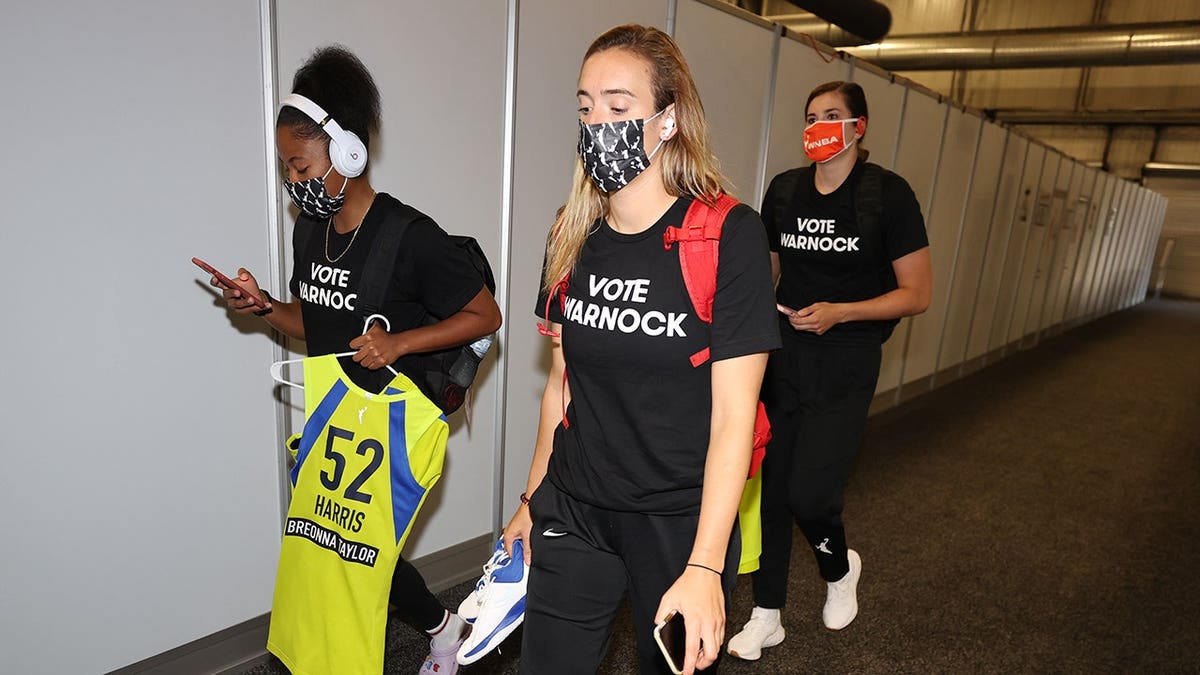Marina Mabrey and Tyasha Harris wear Vote Warnock T-shirts before a game.