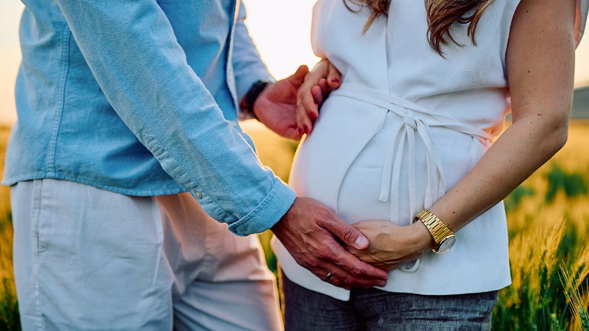 A married couple holds hands and the wife is pregnant