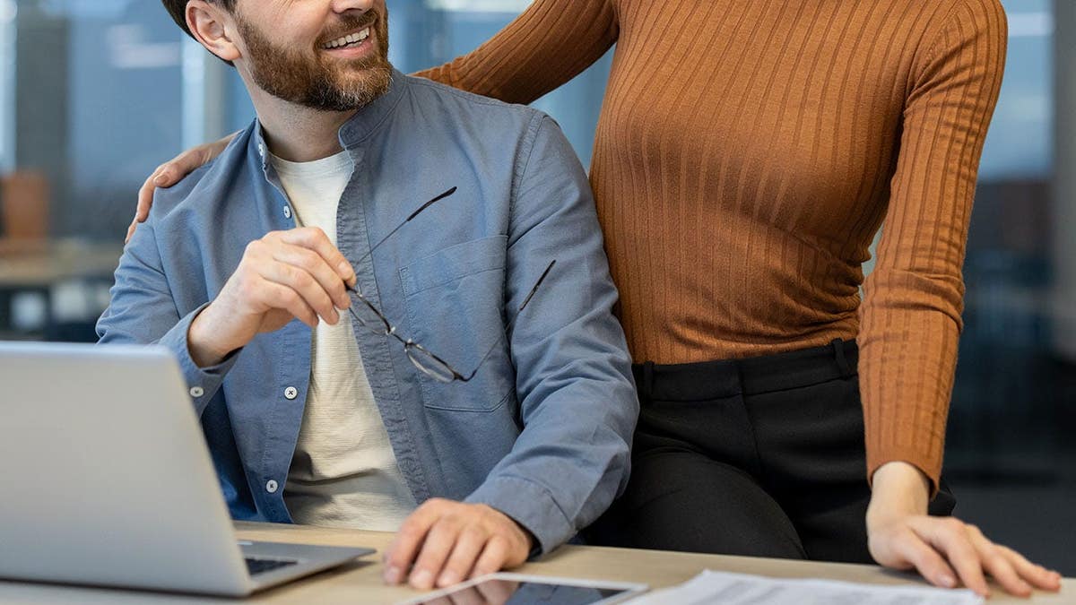 Woman and man interact in an office while colleagues work nearby.