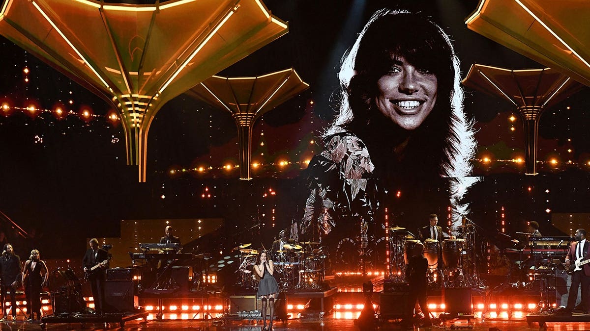 Olivia Rodrigo performs on stage under a photo of Carly Simon during the Rock and Roll Hall of Fame Induction Ceremony.