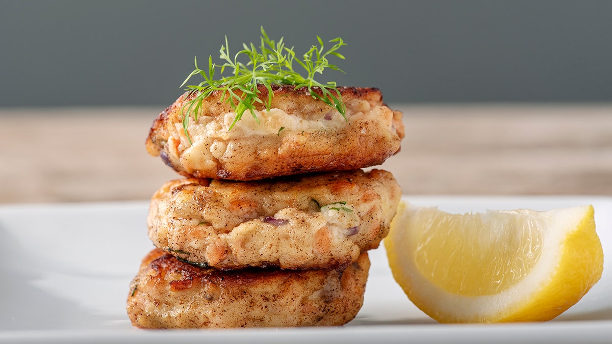 Three salmon cakes stacked on top of each other next to a lemon.