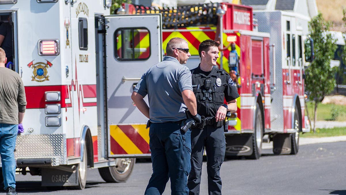 Two Santaquin police officers confer beside a fire truck and ambulance on a residential street.