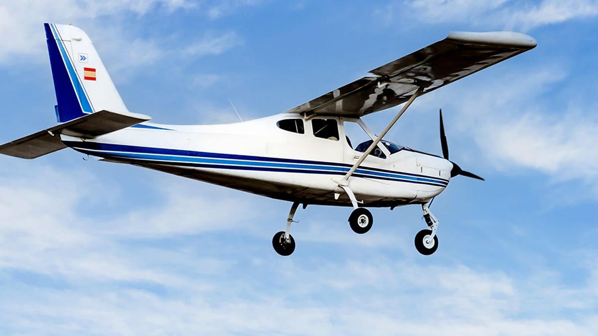 Single-engine ultralight plane flies in a blue sky with white clouds.