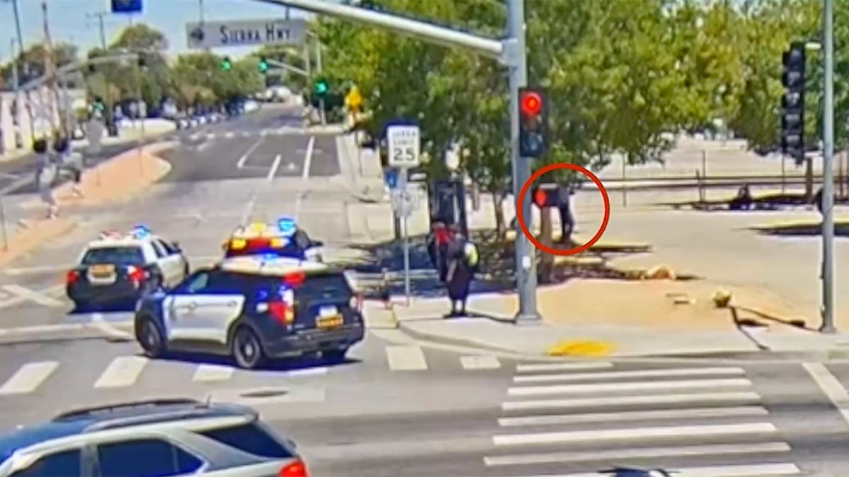 Surveillance camera image shows sheriff's patrol vehicles arriving at an intersection in Lancaster, California, as a person highlighted by investigators stands nearby.