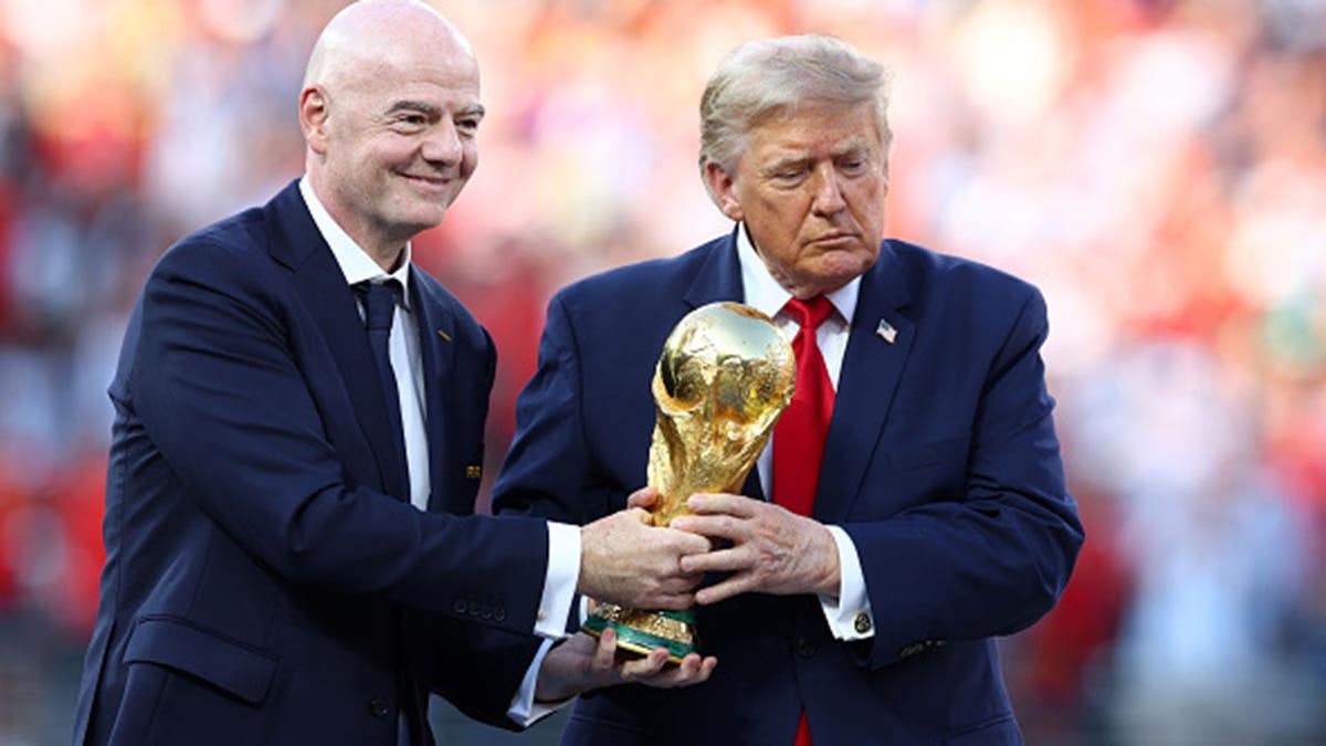 Donald Trump and Gianni Infantino hold the trophy at a soccer stadium.