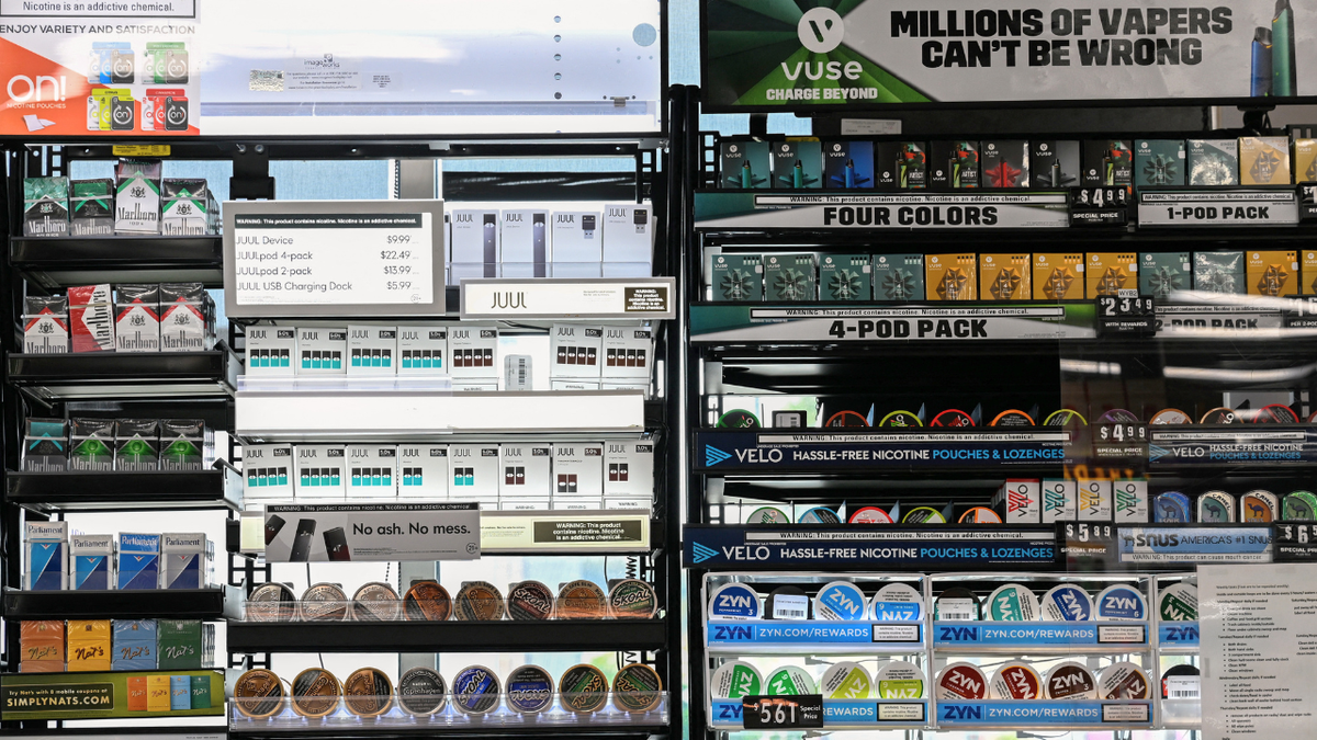 Vaping e-cigarette products are displayed in a convenience store alongside cigarettes, vapes, and other smokeless chewing tobacco products.