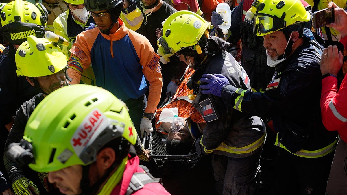 Rescuers carrying man rescued from rubble done a crowd