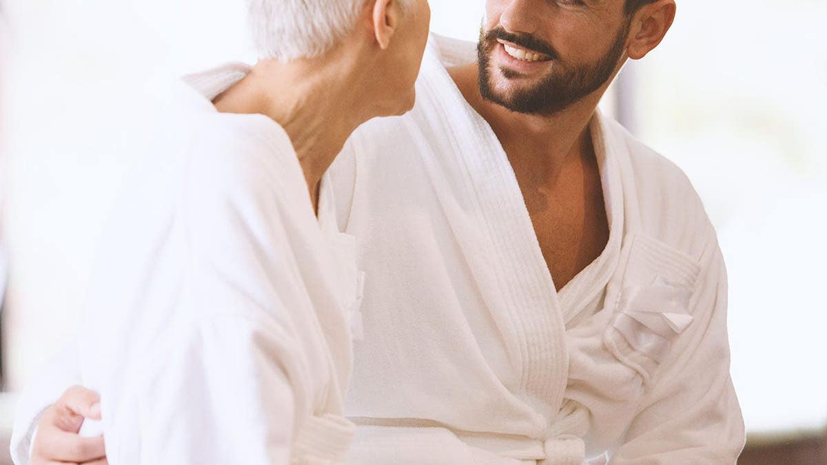 Young man and mature woman sit by the pool in bathrobes.