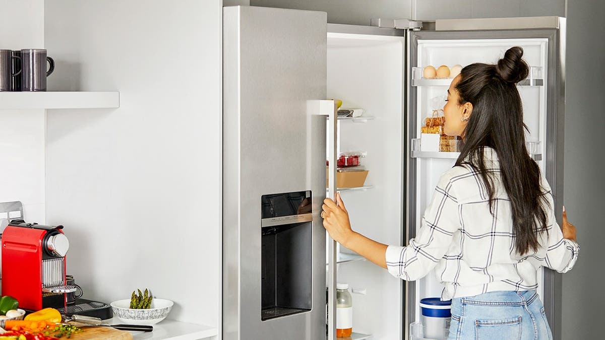 A woman looks at food in a refrigerator.
