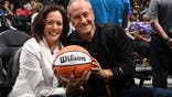 Kamala Harris and Doug Emhoff sit in the arena stands at a basketball game.