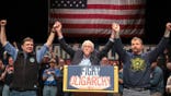 Bernie Sanders standing with Troy Jackson and Graham Platner on a stage.
