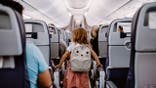 Little girl with backpack stands in the airplane aisle.