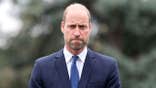 Prince William looking serious in a dark blue suit.