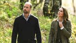 The Prince and Princess of Wales walking together in a forest looking concerned.