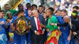 Reece James lifts the FIFA Club World Cup trophy on stage with Donald Trump nearby.
