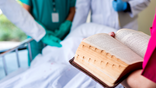 Hospital workers reading a Bible to a patient in a hospital bed.