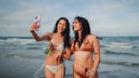 Friends taking a selfie on a beach during summer vacation while holding beer.