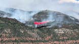 plane dumping red fire retardant in the mountains as smoke billows from the wildfire