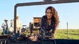 Jess Pryles handles barbecue ribs with gloves and a tong while standing near some cowboys.