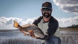 man in a marsh holds up a fish