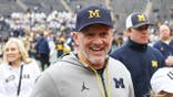Kyle Whittingham smiles while walking off the field at Michigan Stadium.