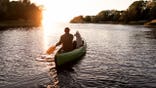 Man and dog paddle a canoe on a river during sunset.