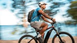 man riding an electric mountain bike along the seaside, wearing a safety helmet.