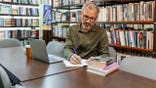 Man writes notes at a table in a library.