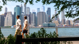 People are seen walking by the New York City skyline.
