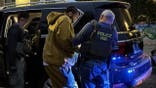 A suspect is led out of a vehicle, guided by a law enforcement agent