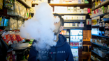A person exhales vapor while using an electronic cigarette device at a smoke shop in New York.