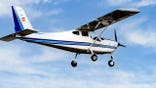 Single-engine ultralight plane flies in a blue sky with white clouds.
