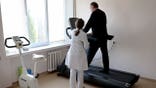 A doctor observes a man walking on a treadmill.