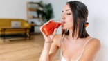 A woman drinks tomato juice with her eyes closed.