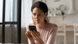 Woman looks at cell phone while sitting on a sofa.