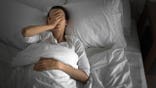 Woman lies in bed appearing sick and fatigued.
