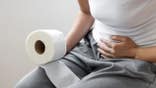 An unrecognizable woman seated on a toilet holding toilet paper.