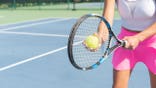 Female player holds a racket and ball near the net on a tennis court.
