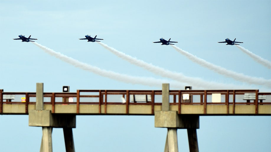 The U.S. Navy Blue Angels fly next to each other over a pier. 