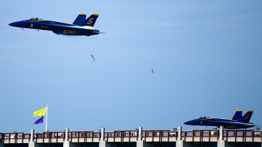 Two Blue Angels jets fly over a bridge.