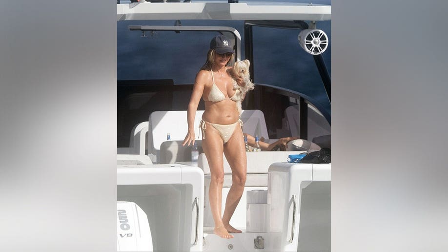 Heidi Klum in a cream-colored bikini holding a dog while on a yacht.