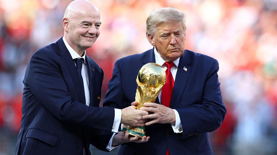 Donald Trump and Gianni Infantino hold the trophy at a soccer stadium.