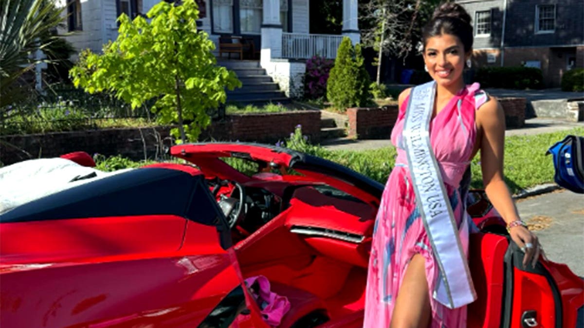 Brittany Boltinhouse wearing a pink dress and Miss Wilmington, USA sash in front of a red sports car