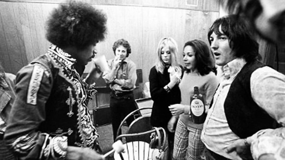 Jimi Hendrix holding a beer in a recording studio speaking with Eric Barrett.