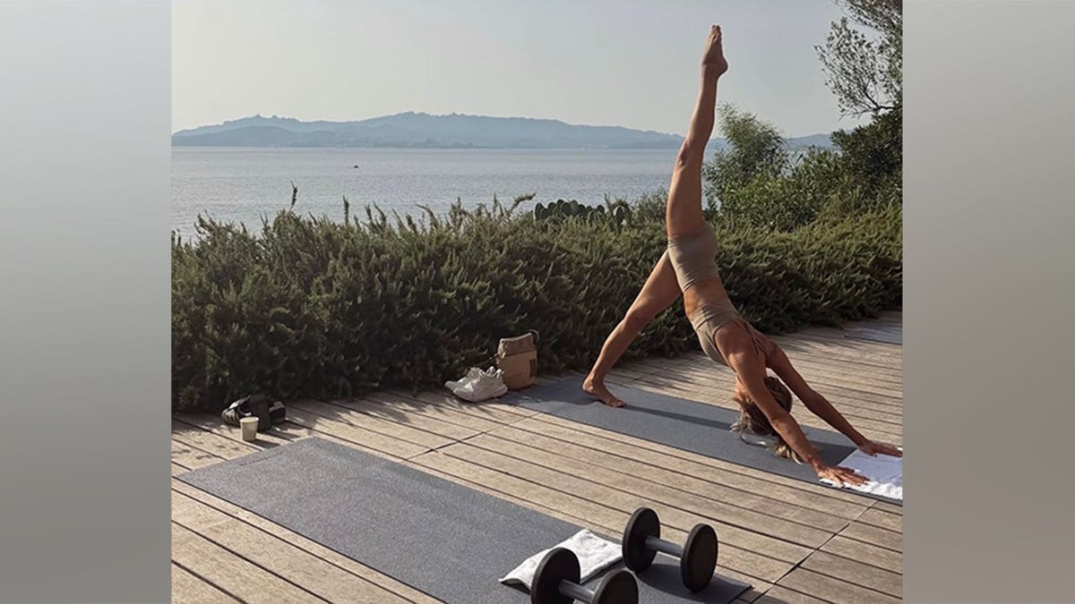 Julianne Hough practices yoga on a wooden deck overlooking the water in Sardinia.