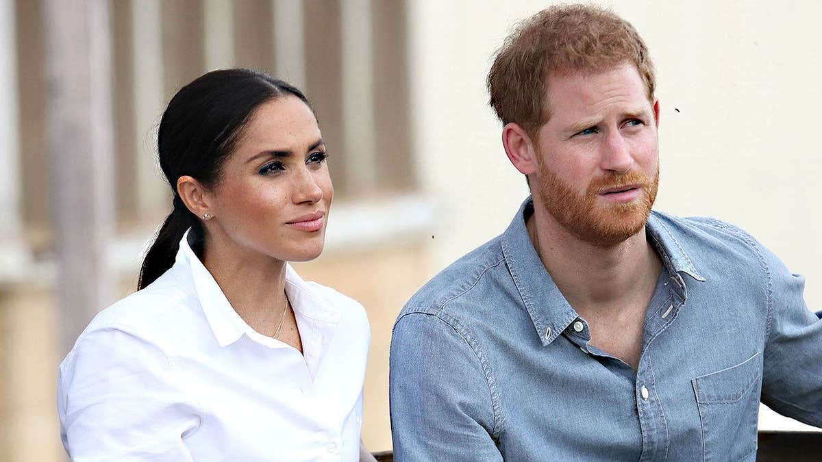 Meghan Markle in a white shirt and Prince Harry in a blue shirt looking concerned.