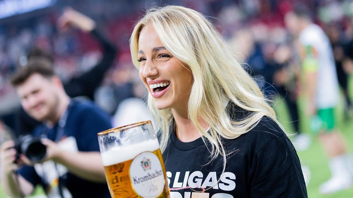 Ana Maria Markovic celebrates holding a large glass of beer.