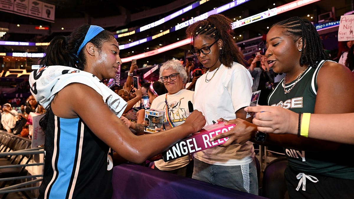 Angel Reese signs memorabilia for a fan after a game.