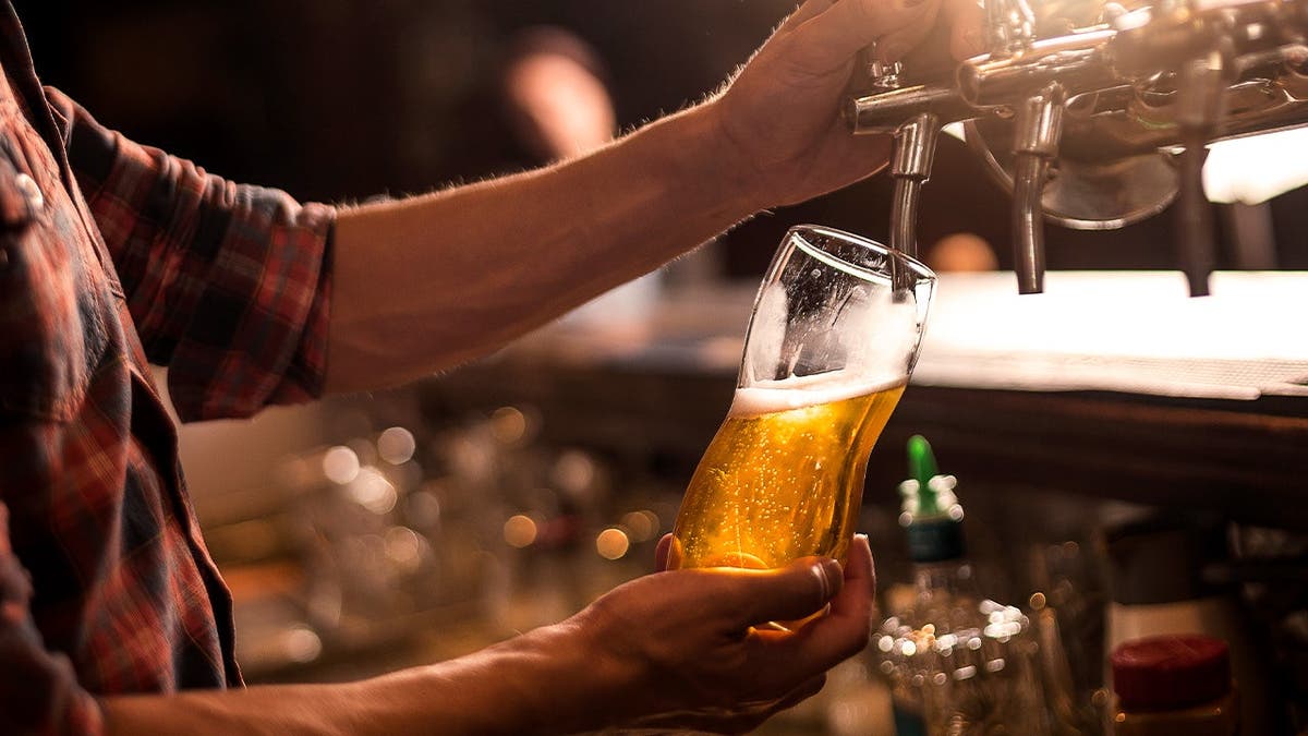 A bartender uses a tap to fill a glass with beer.